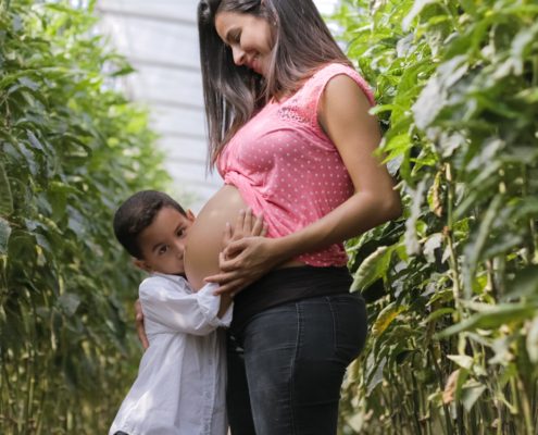 Pregnancy woman with young boy kissing her pregnant belly and looking at the camera