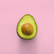 Half an avocado with seed in the centre on a pink background