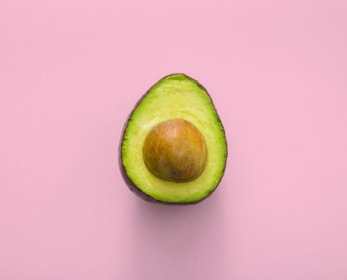 Half an avocado with seed in the centre on a pink background