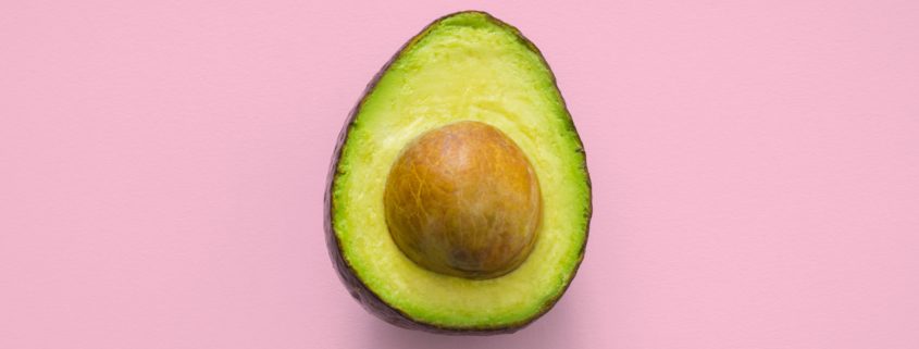 Half an avocado with seed in the centre on a pink background